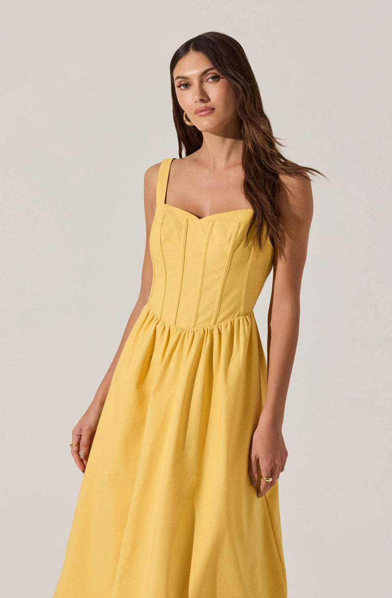 A woman is wearing a bright yellow sleeveless dress with spaghetti straps, featuring a fitted bodice with vertical seam details and a gathered, full skirt.