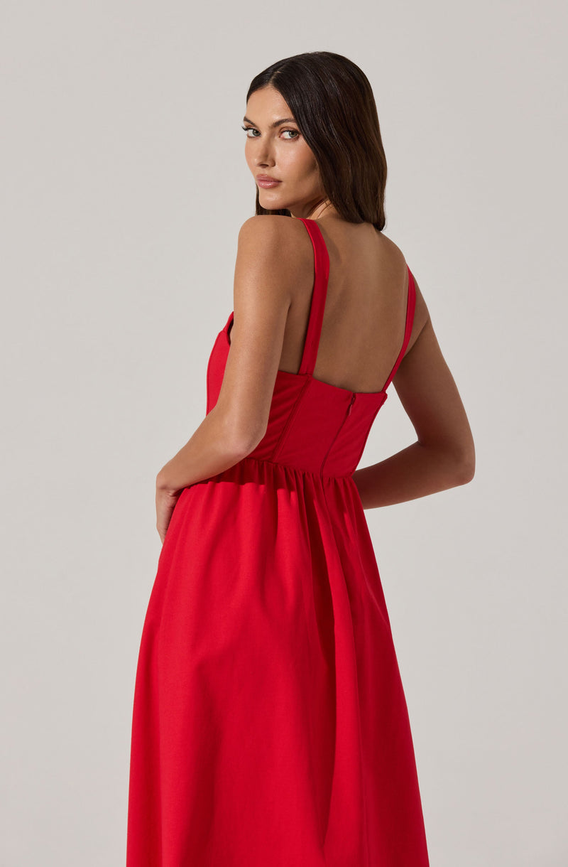 A woman is wearing a sleeveless, floor-length red dress with fitted bodice and spaghetti straps. The back of the dress features a low, open style with a visible zipper and gathered fabric at the waist.