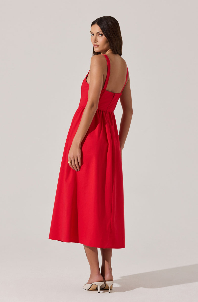 A woman is wearing a sleeveless, ankle-length dress in a bright red color. The dress features thin shoulder straps and a fitted bodice that transitions into a gathered, flowy skirt. She is paired with white high-heeled shoes.