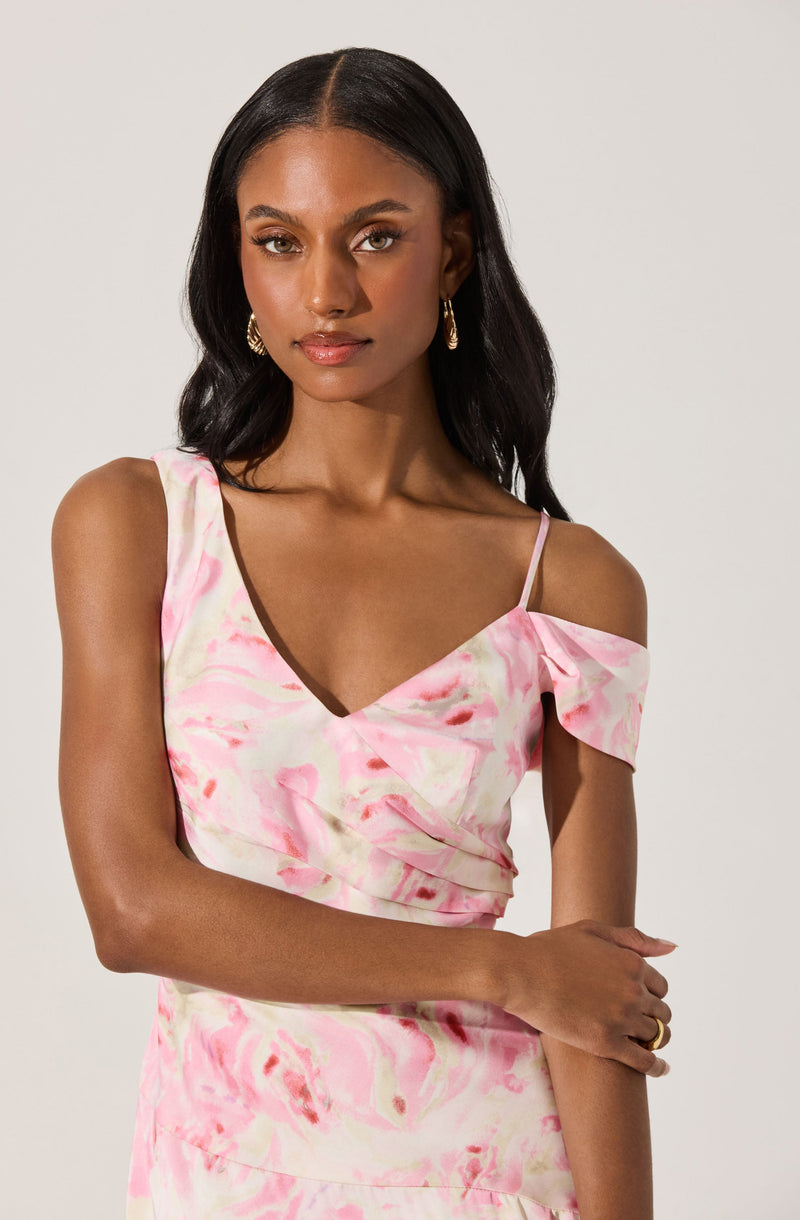 A woman is wearing a sleeveless, V-neck top with a pink and white marbled pattern. The top has thin spaghetti straps and a ruffled detail on one shoulder, with a cold shoulder design on the other side.