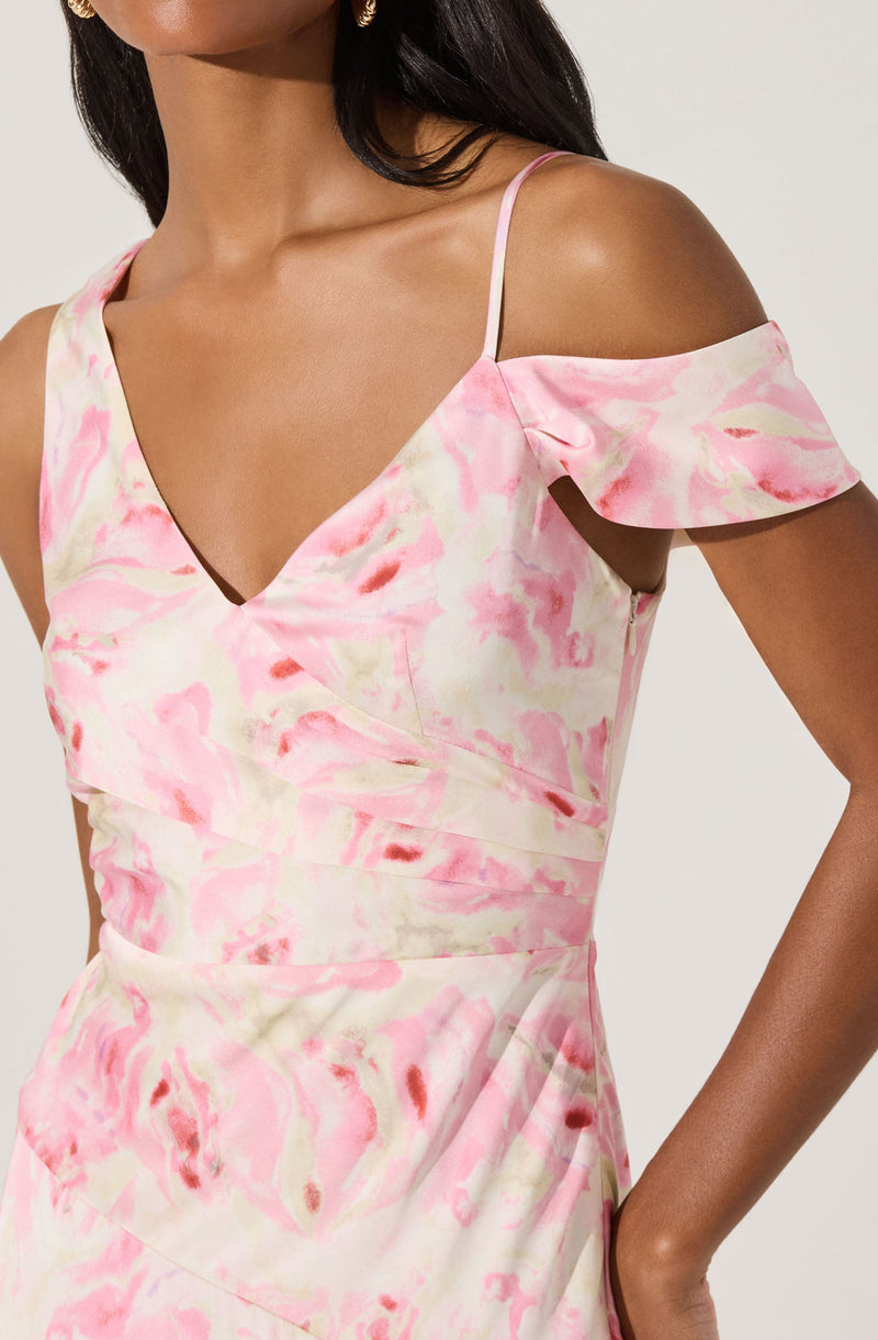 The dress features a pink and cream watercolor-like print. It has thin spaghetti straps, a deep V neckline, and an off-the-shoulder ruffle detail on one side. The fabric appears smooth and lightweight, creating a soft, feminine look.