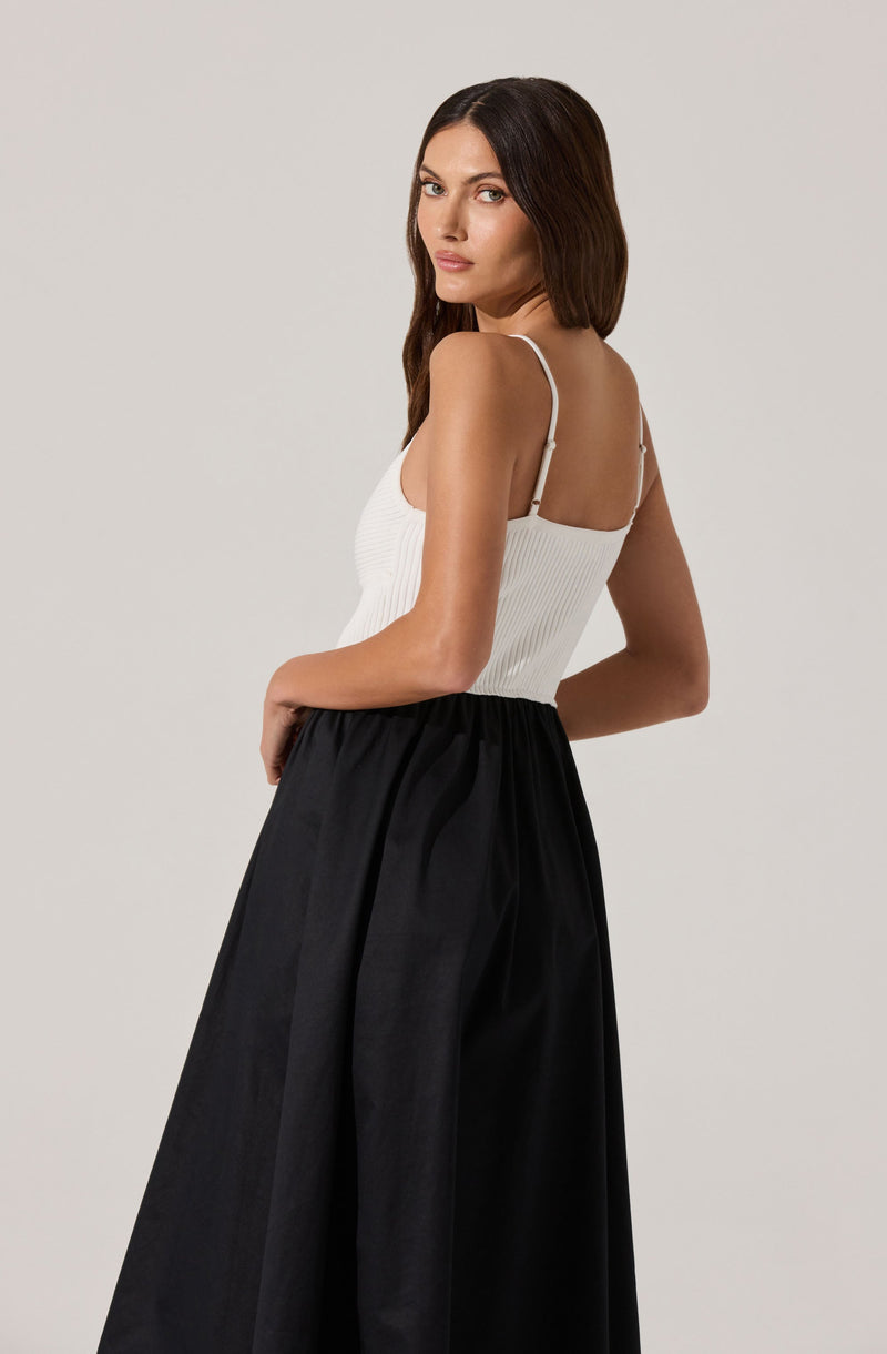 A woman is wearing a white ribbed tank top with thin spaghetti straps and a pair of high-waisted, wide-leg black pants.