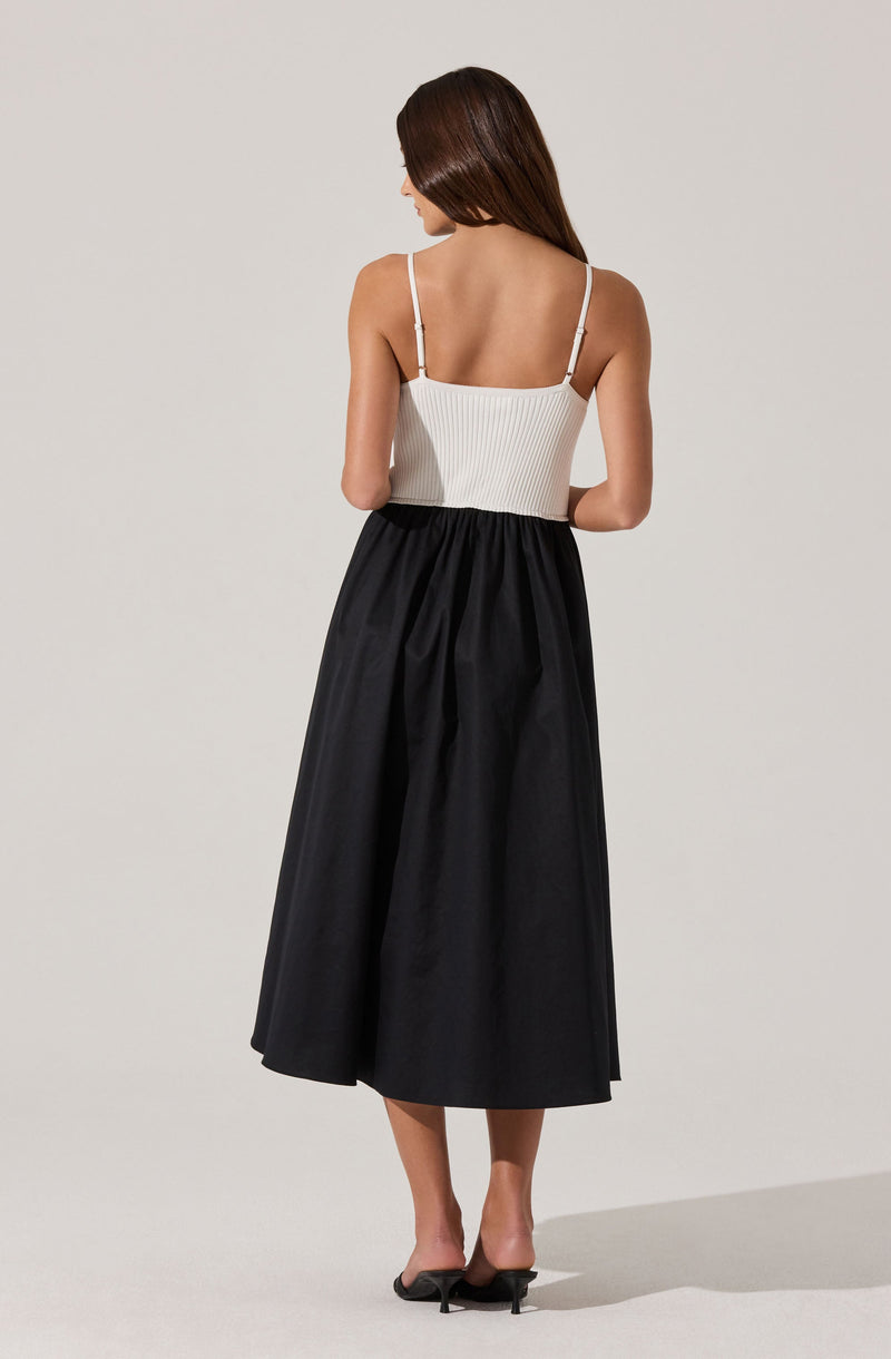 A woman is wearing a white ribbed tank top with thin spaghetti straps and a high-waisted, full-length black skirt that has a gathered, slightly pleated design. She is also wearing black open-toe high-heeled shoes.