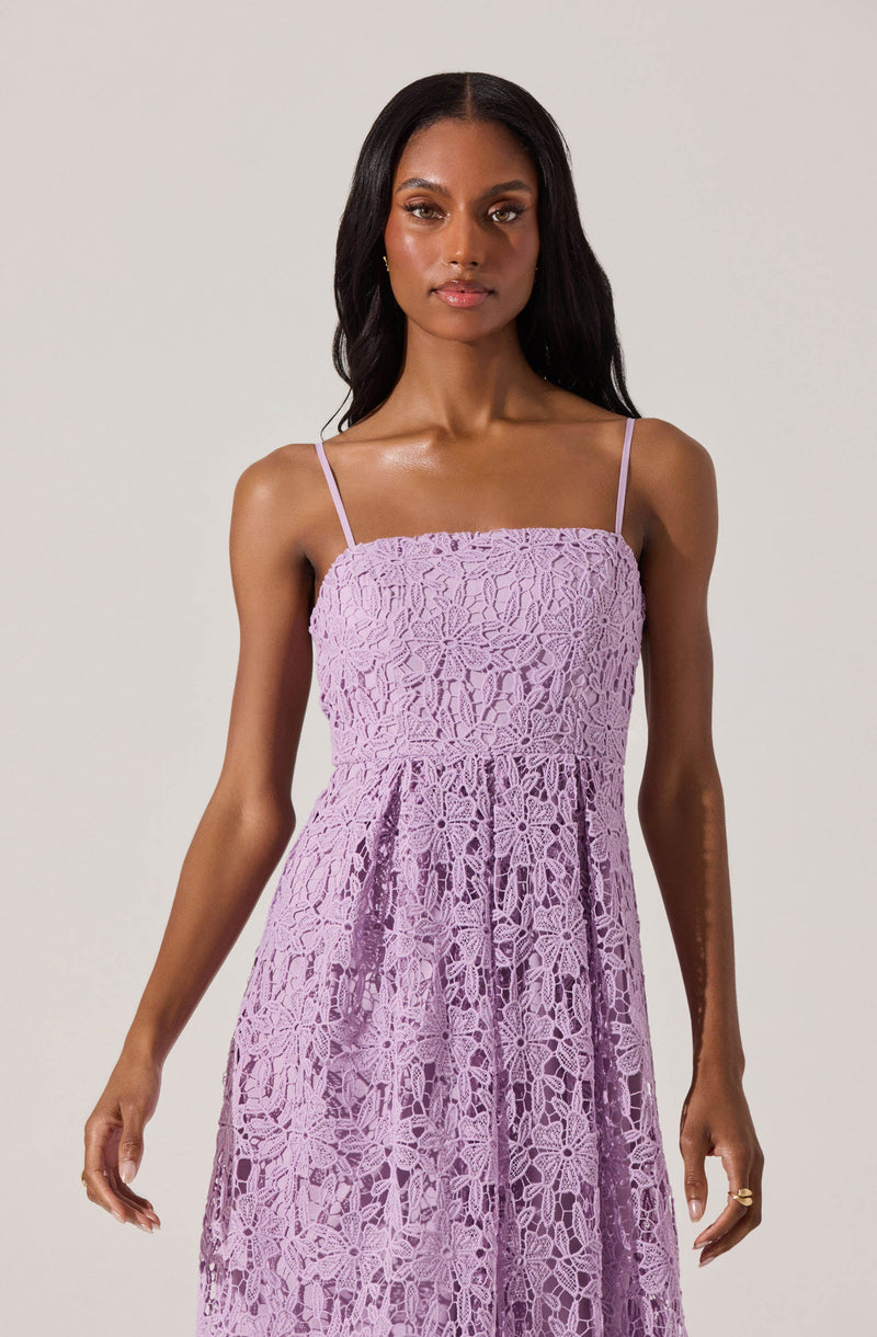 A woman wearing a sleeveless, lavender-colored dress with thin spaghetti straps. The dress features an intricate lace pattern throughout, with a fitted bodice and a gathered skirt.