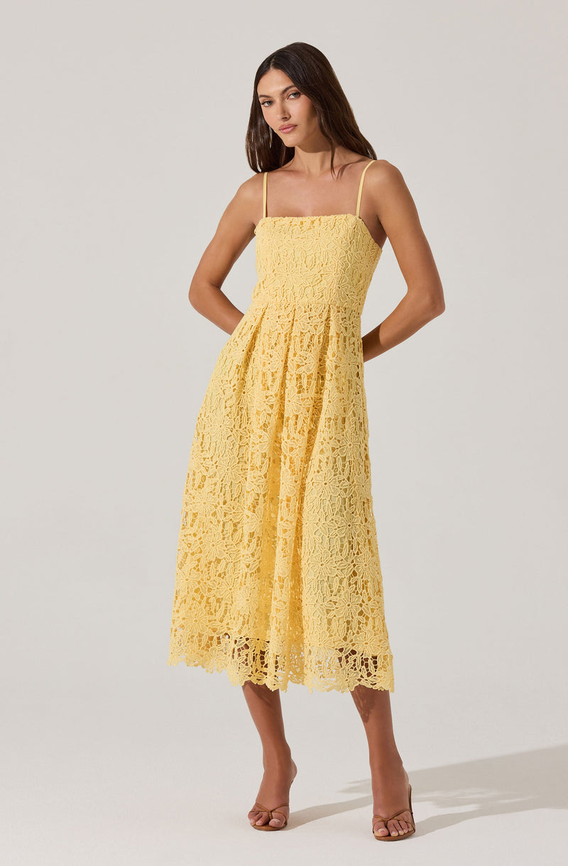 A woman is wearing a yellow lace dress with spaghetti straps. The dress has a fitted bodice and a flowing, mid-length skirt with intricate lace patterns throughout. She pairs the dress with nude open-toe heels.