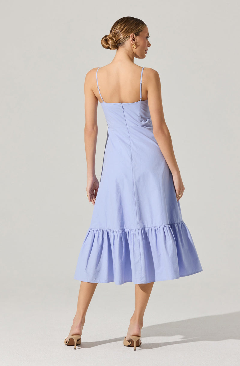 A woman is wearing a light blue midi dress with thin spaghetti straps. The dress has a fitted bodice and a ruffled hem at the lower part of the skirt. She is also wearing beige high-heeled shoes.