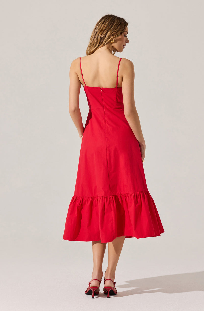 A woman is wearing a sleeveless, red midi dress with thin spaghetti straps and a fitted bodice. The dress features a gathered ruffle hem that falls below the knees. She pairs the outfit with red high-heeled sandals that have ankle straps.