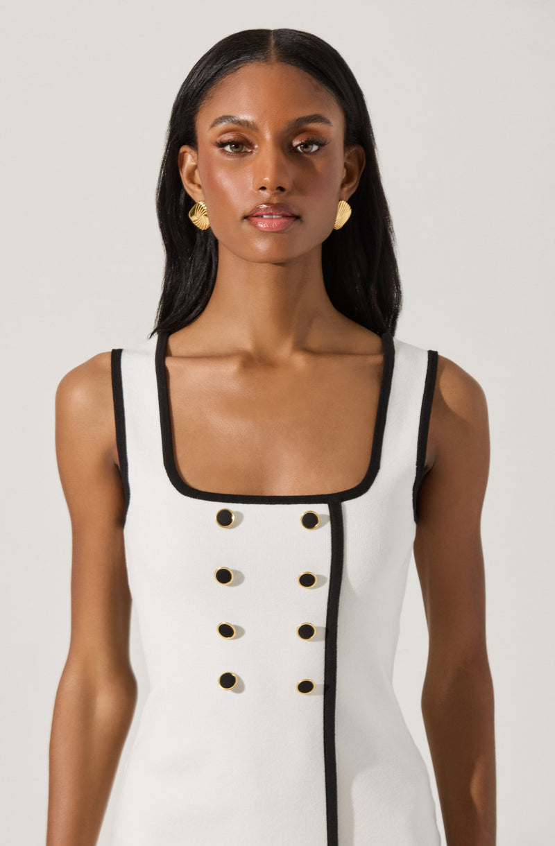 A woman is wearing a sleeveless, white dress with black trim around the square neckline and armholes. The dress features a double row of black buttons with gold accents running vertically down the front.