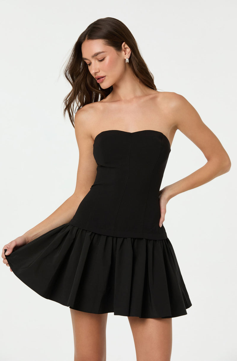 A woman is wearing a strapless black dress with a fitted bodice and a flared, pleated skirt.