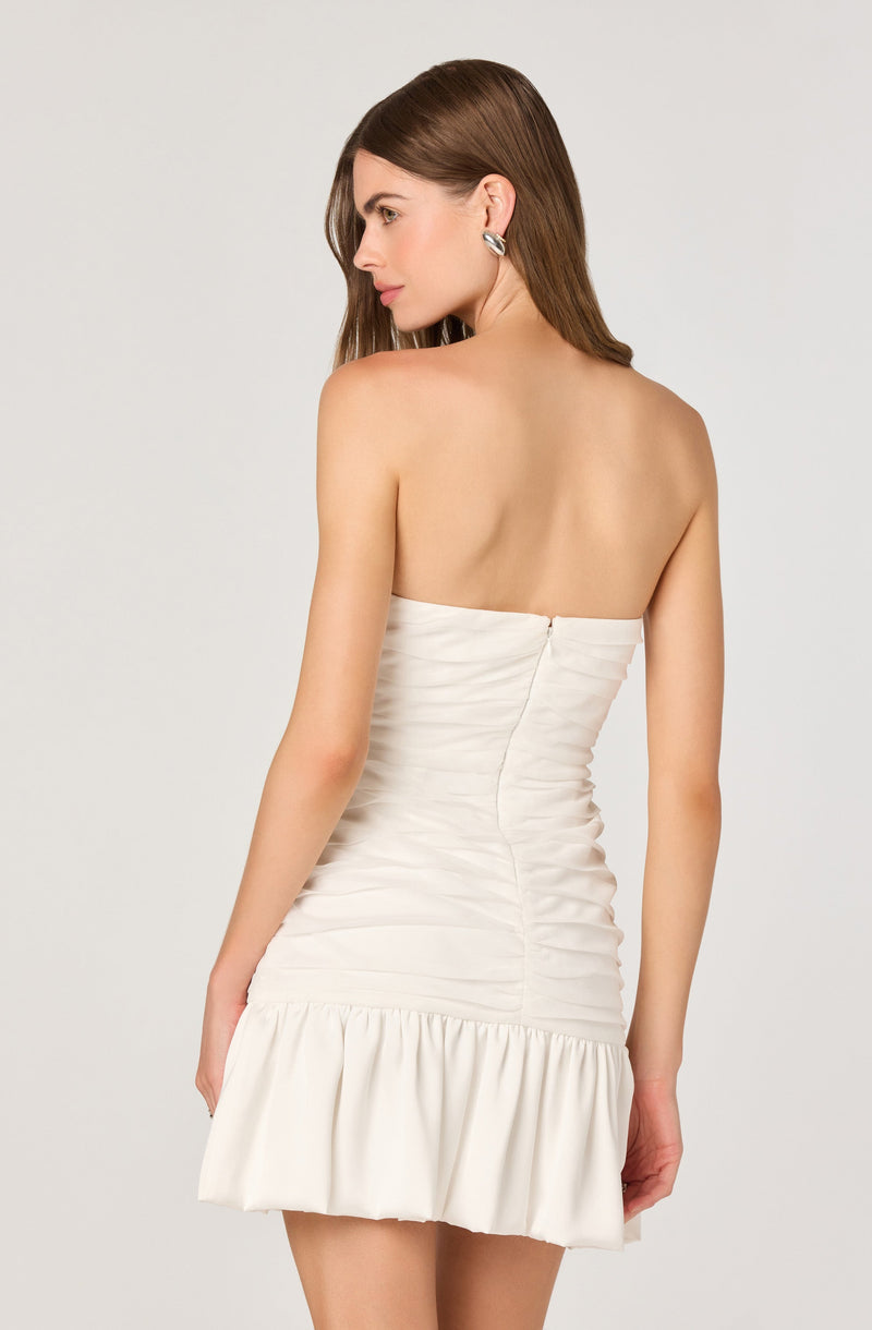 A woman is wearing a strapless white dress with a ruched bodice and a gathered ruffle hem.