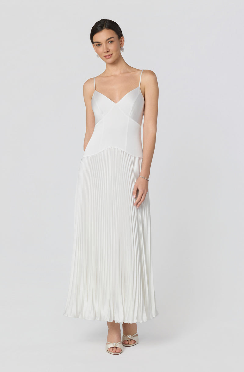 Girl in a white sleeveless dress with spaghetti straps and pleated skirt.