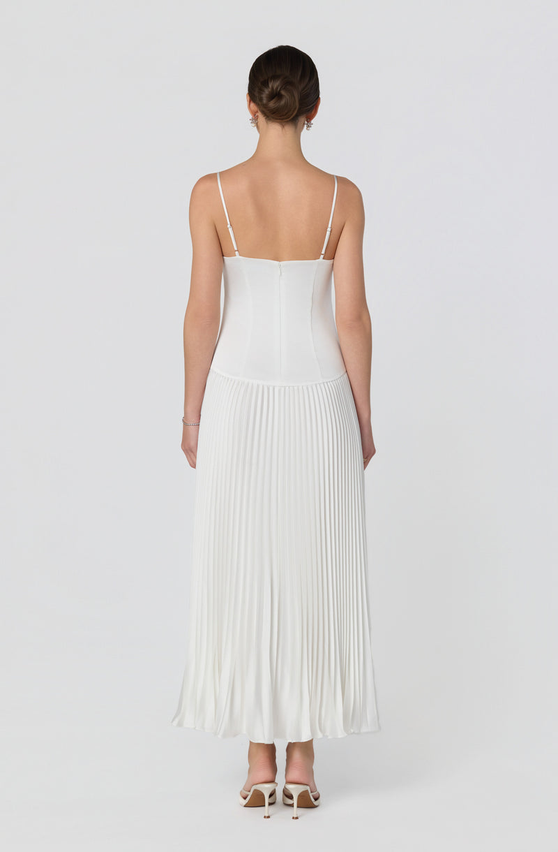 Woman wearing a white sleeveless dress with thin straps and a pleated skirt.
