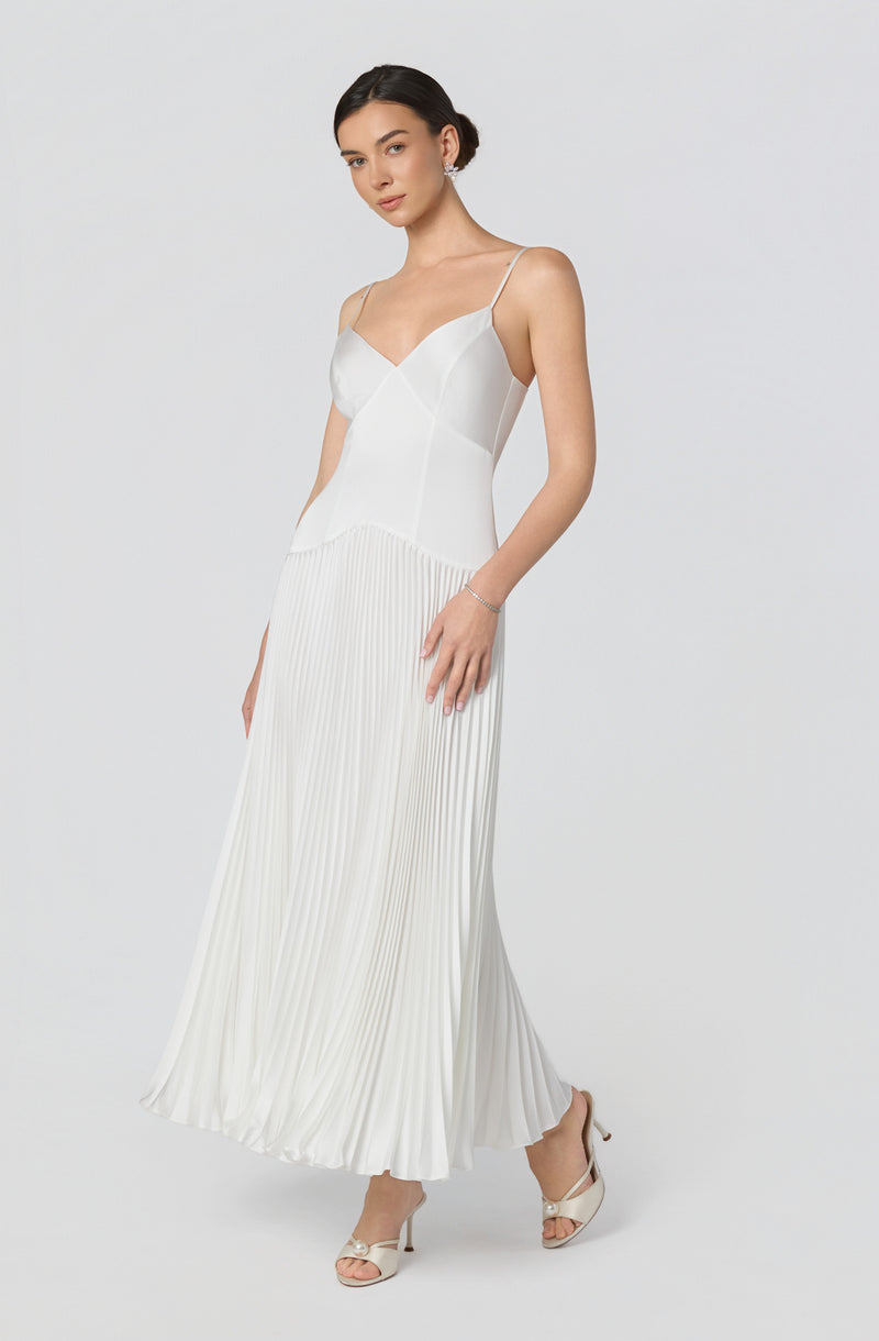 Woman in a white pleated maxi dress with spaghetti straps and open-toe heels.