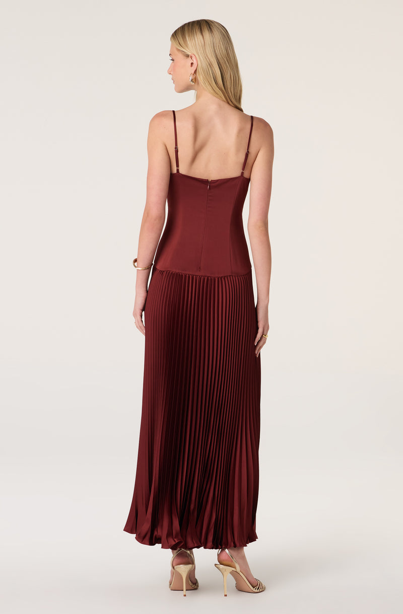 Woman in a burgundy satin slip dress with thin adjustable straps and a pleated skirt.