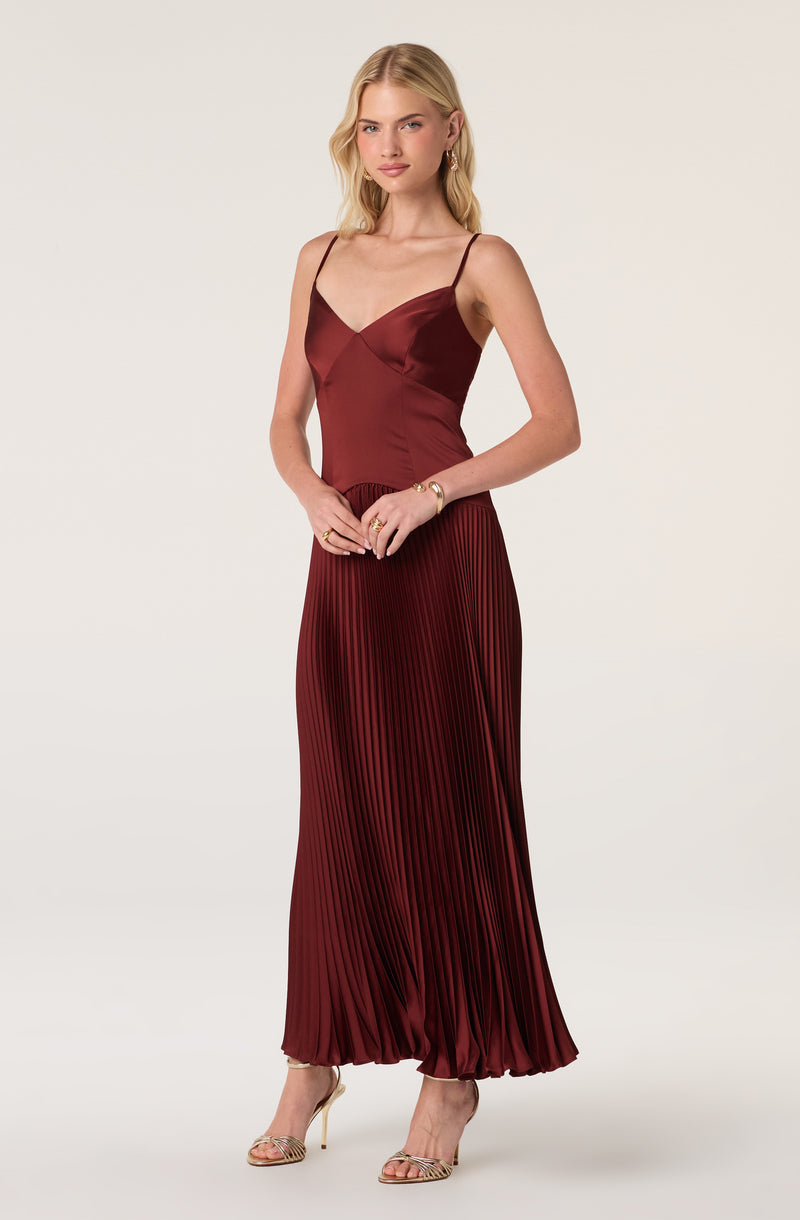 Woman in a burgundy satin camisole and pleated maxi skirt with thin straps and high heels.