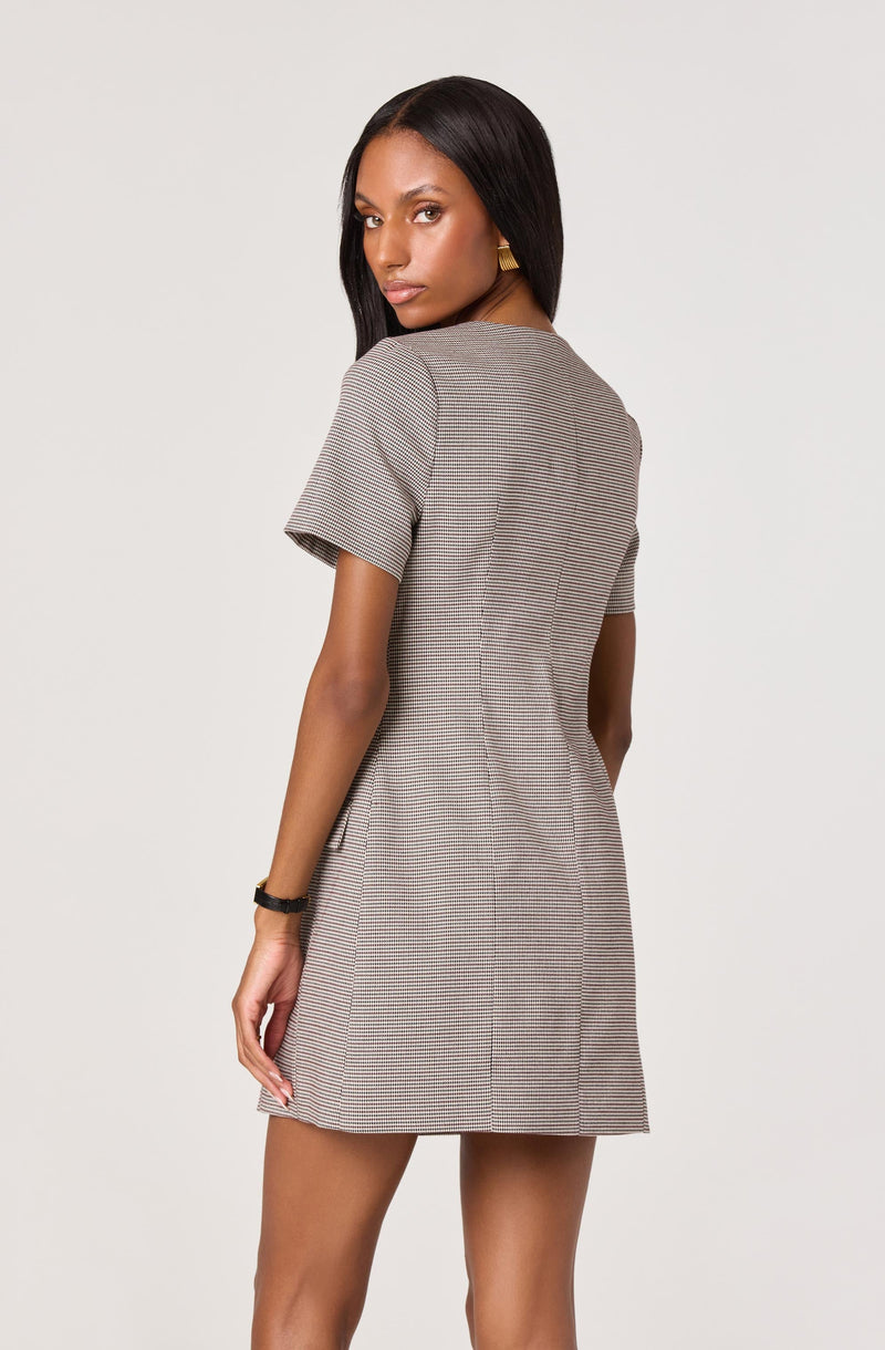 A woman is wearing a short-sleeved, knee-length dress with a fitted waist. The dress features a small checkered pattern with neutral tones.
