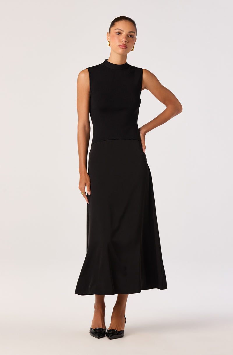 Woman wearing a sleeveless black turtleneck top and a long black skirt with a slit.