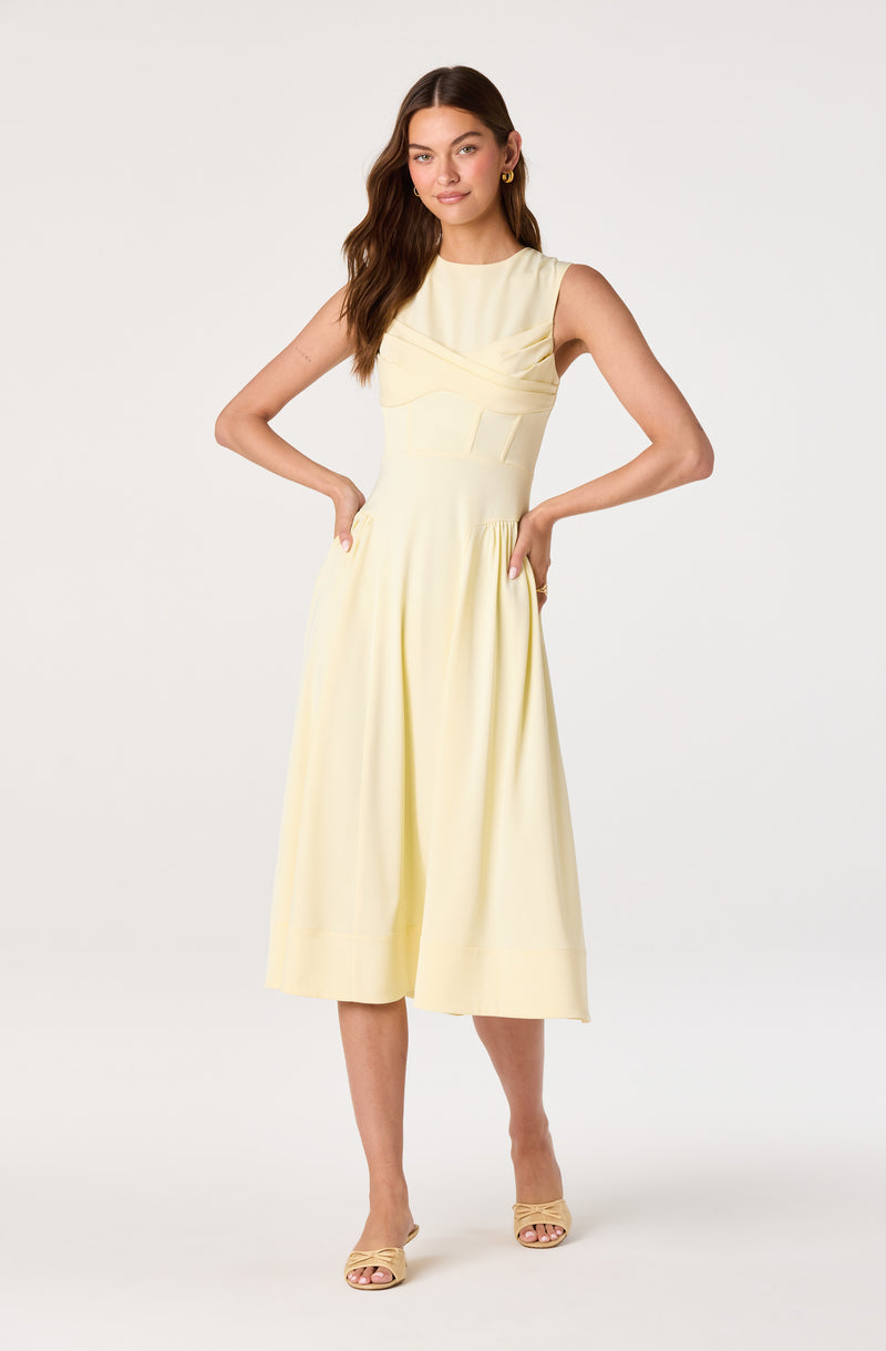 Woman in a sleeveless, cream-colored midi dress with pleats and a fitted waist.