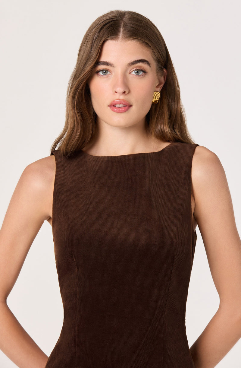 A woman is wearing a sleeveless, fitted, brown dress made of a textured fabric. She has on gold, circular earrings with a decorative pattern.
