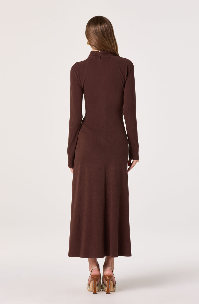 A woman is wearing a long, fitted, brown dress with a high neckline and long sleeves. The dress extends down to her ankles. She is also wearing high-heeled shoes with a beige and gold pattern.