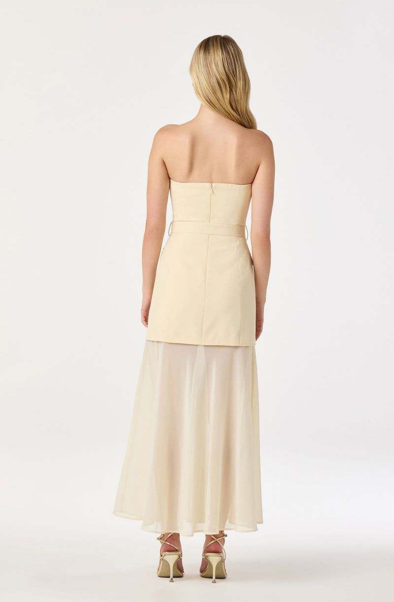 Back view of a woman wearing a strapless, beige dress with a fitted top and flowing skirt.