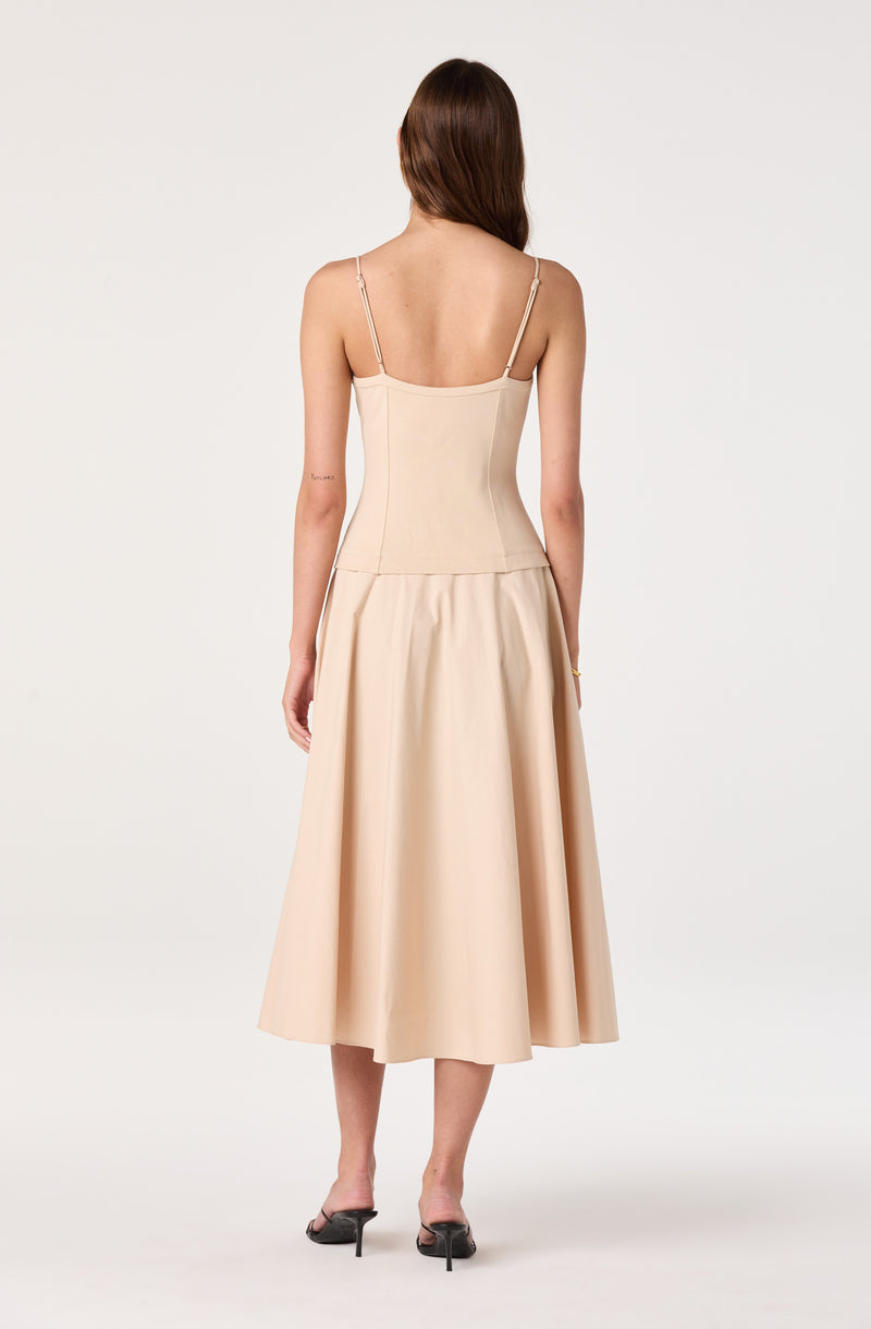 Back view of a woman wearing a beige sleeveless top with spaghetti straps and a matching long, pleated skirt.