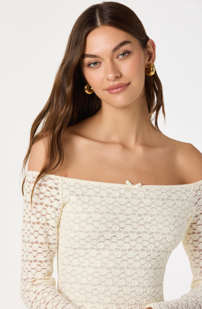 Woman wearing an off-shoulder cream textured knit sweater with long sleeves and gold hoop earrings.