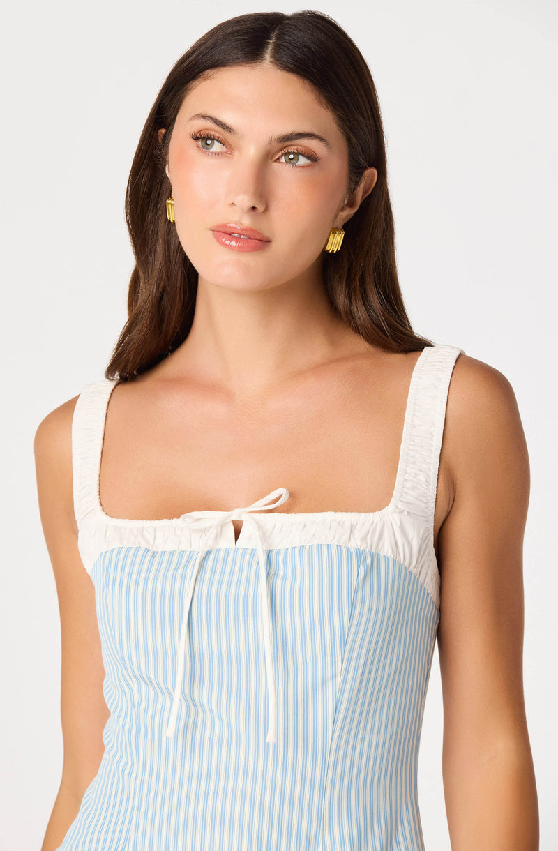 Woman wearing a sleeveless top with white and blue pinstripes and cream-colored straps and bow.