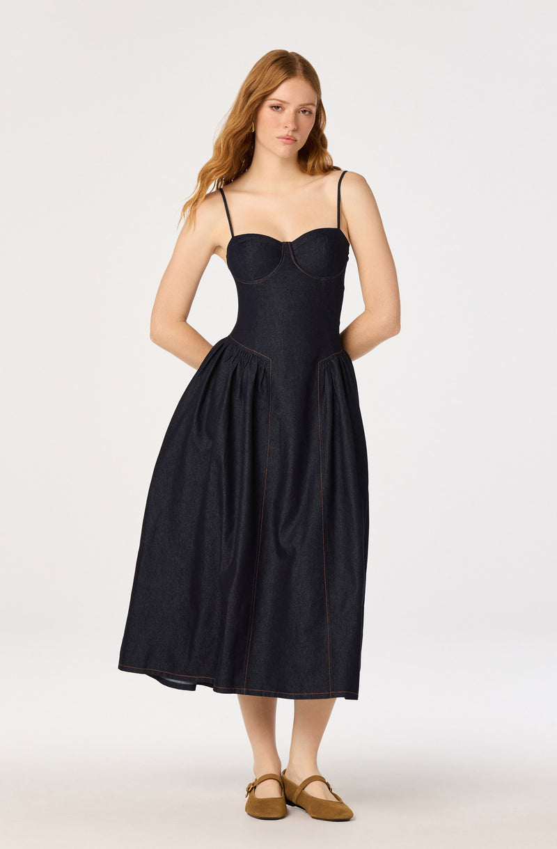 Woman in a dark denim dress with spaghetti straps, fitted bodice, and full skirt.