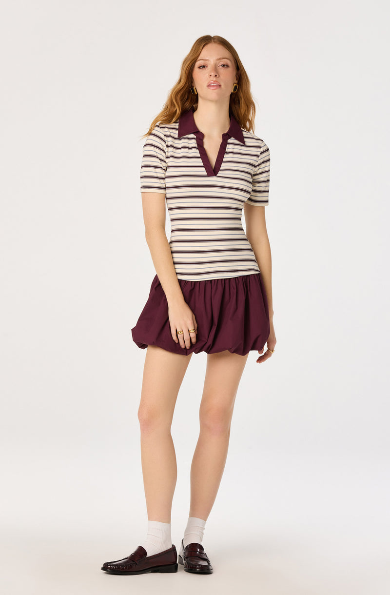 Woman wearing a striped polo shirt with a burgundy collar and trim, and burgundy bubble shorts.