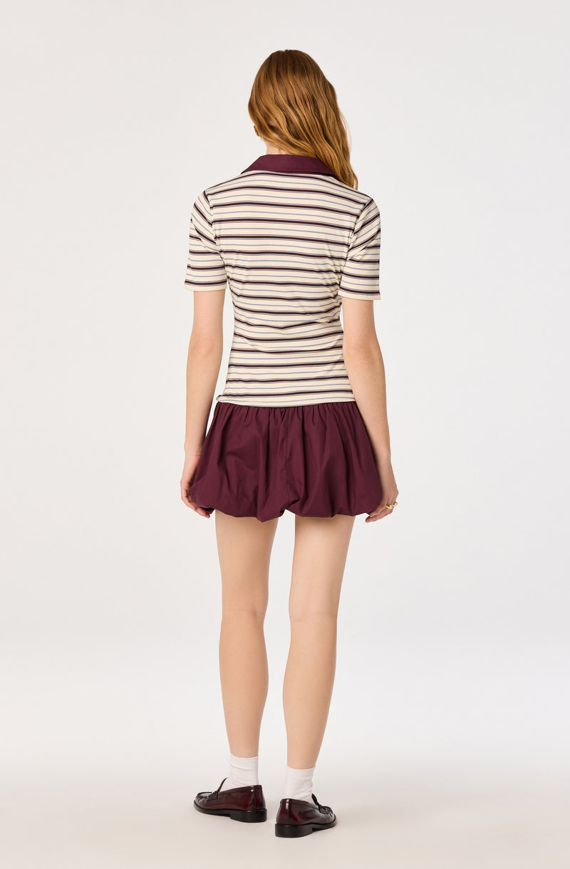 Woman wearing a striped short-sleeve shirt, burgundy bubble skirt, socks, and loafers.
