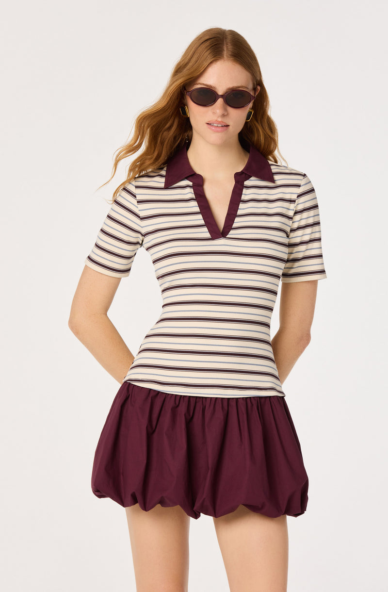Woman in a striped polo shirt with burgundy collar and trim, and burgundy bubble skirt.