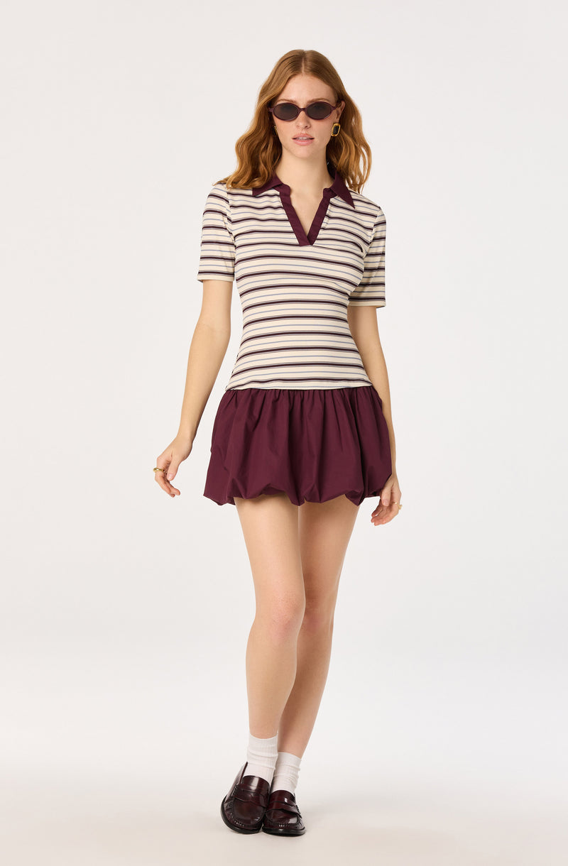 Woman in striped top with burgundy trim, matching burgundy bubble skirt, sunglasses, and loafers.