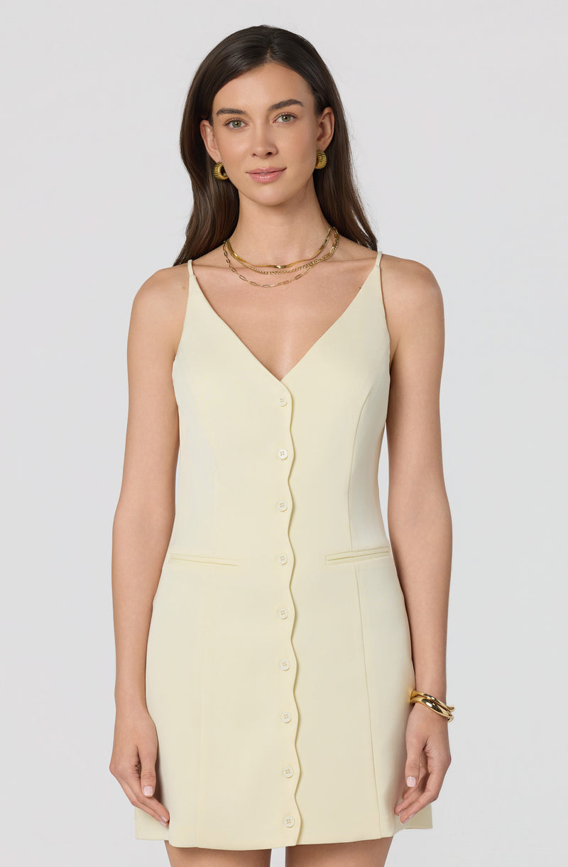 Woman in a cream sleeveless dress with a front button closure and fitted silhouette.