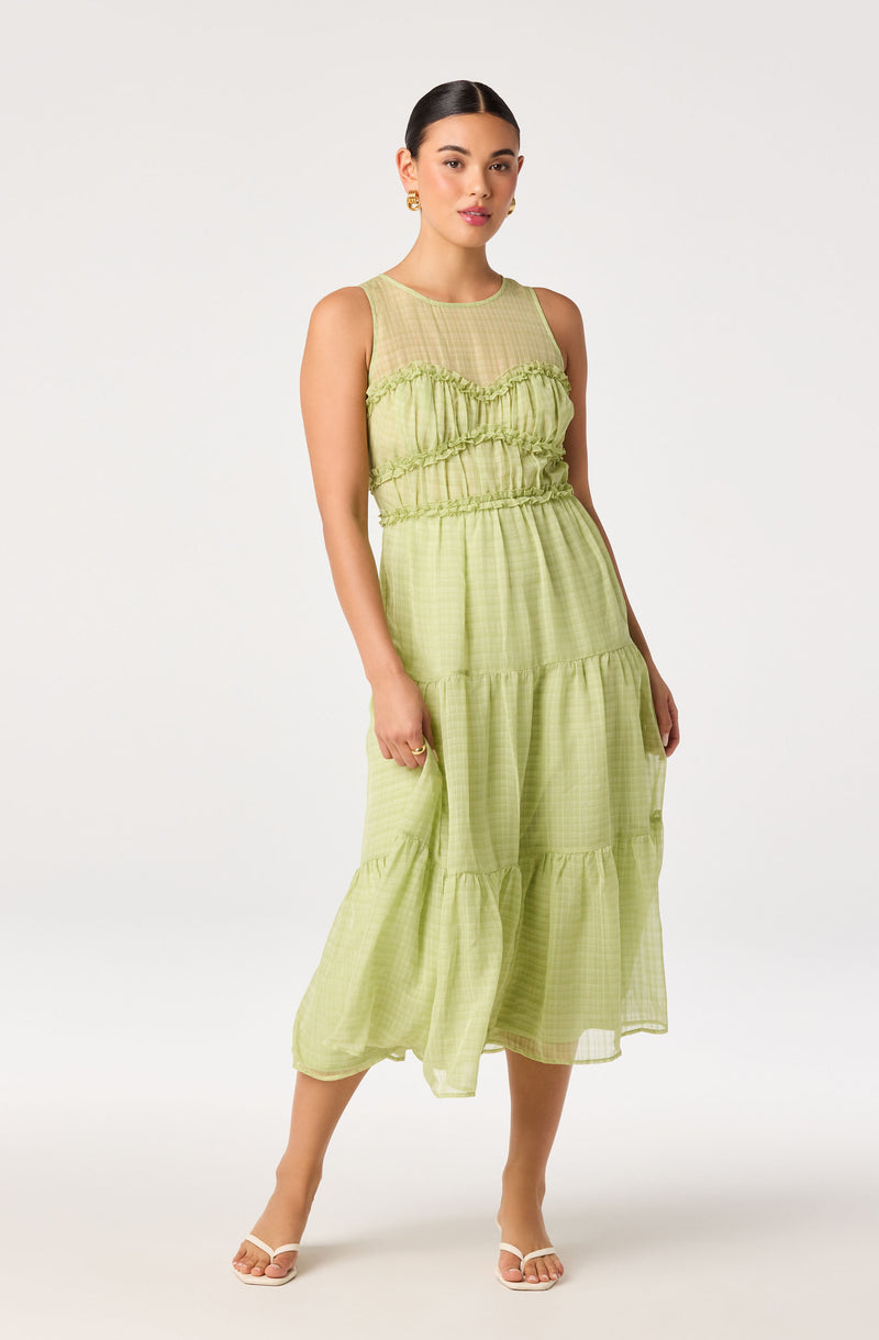Woman wearing a sleeveless, light green, tiered, semi-sheer maxi dress with a ruffled bodice.