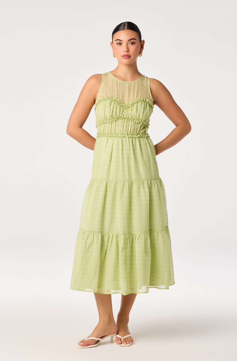 Woman in a light green, sleeveless, tiered midi dress with ruffled details.