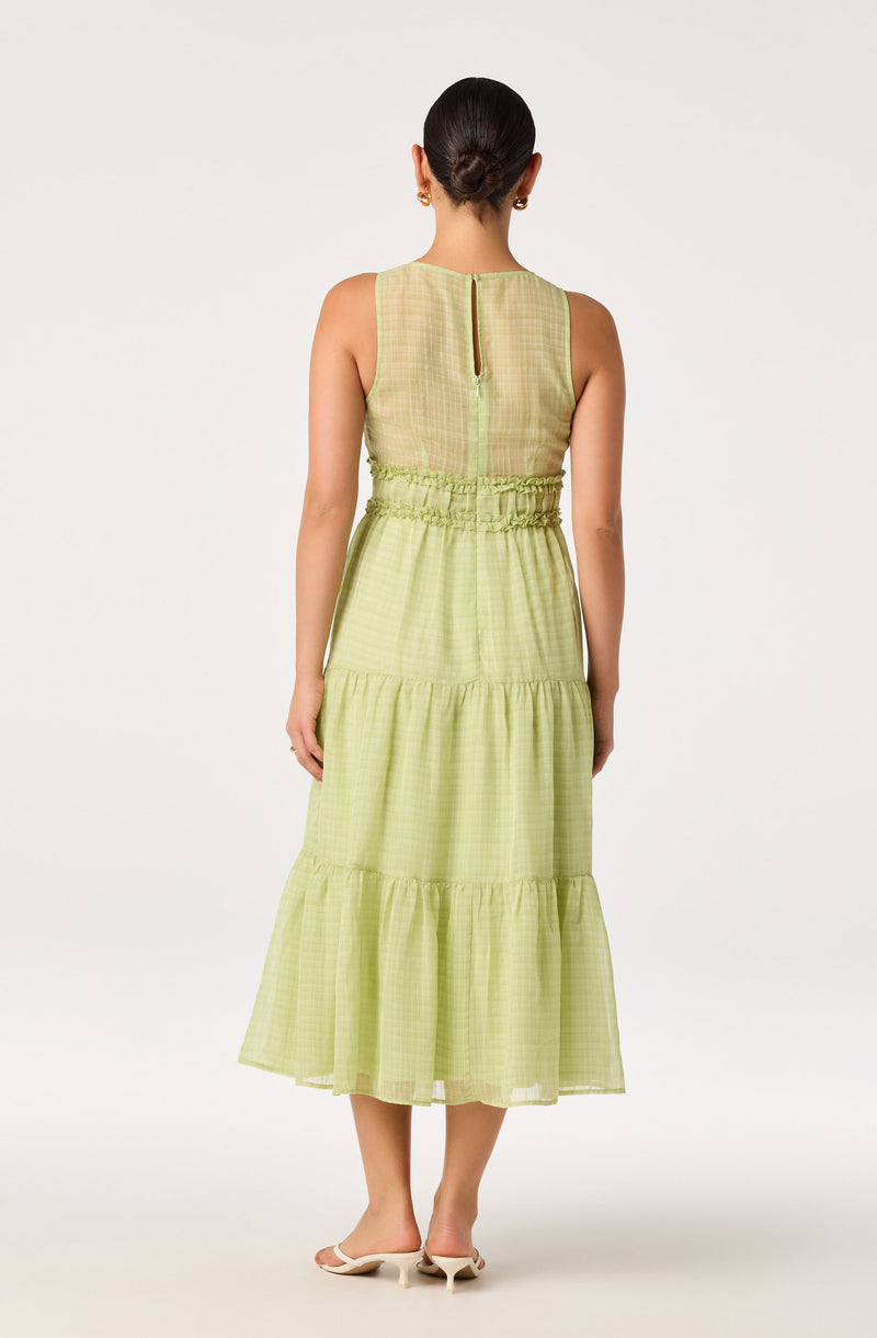Back view of a woman wearing a sleeveless, light green, tiered dress with a vertical slit at the back.