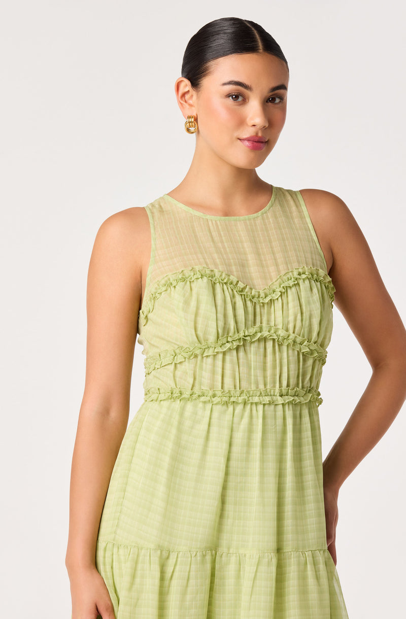 Girl wearing a sleeveless, lime green dress with a sheer top and ruffled details.