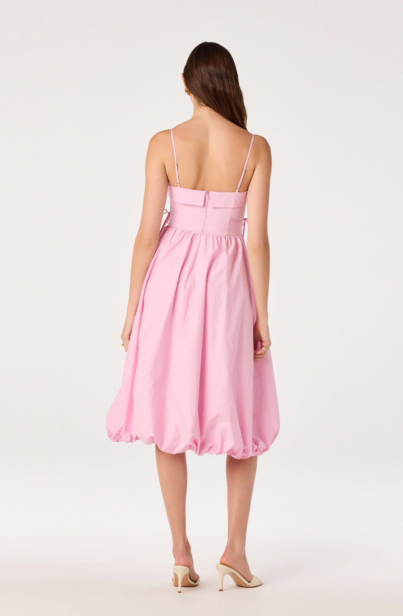 Woman in pink bubble-length dress with spaghetti straps and nude heels, facing away.
