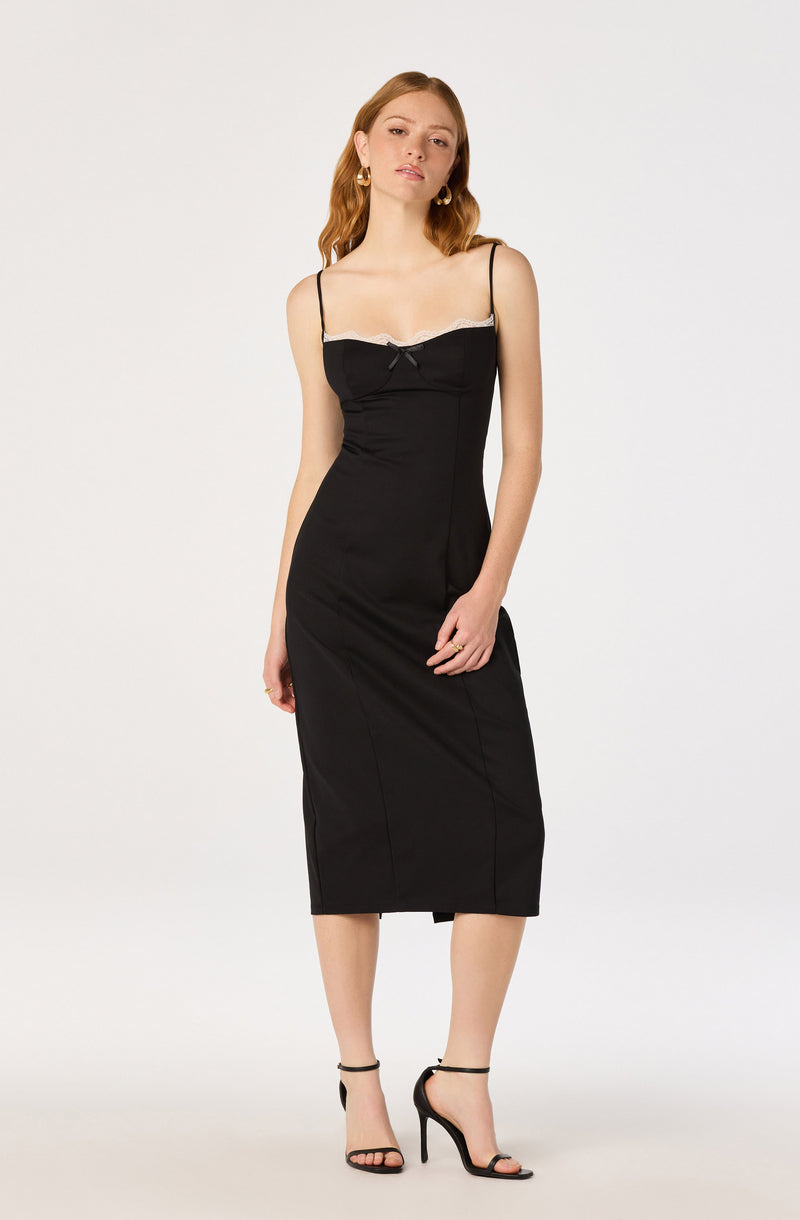 Woman in a black slip dress with white lace trim and spaghetti straps, wearing black high heels.