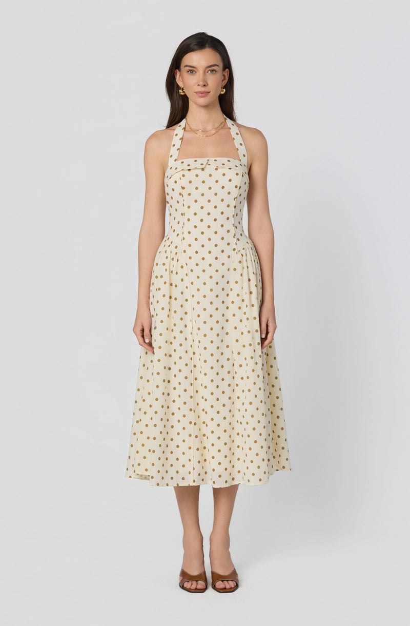 Woman wearing a white dress with beige polka dots and a halter neckline.