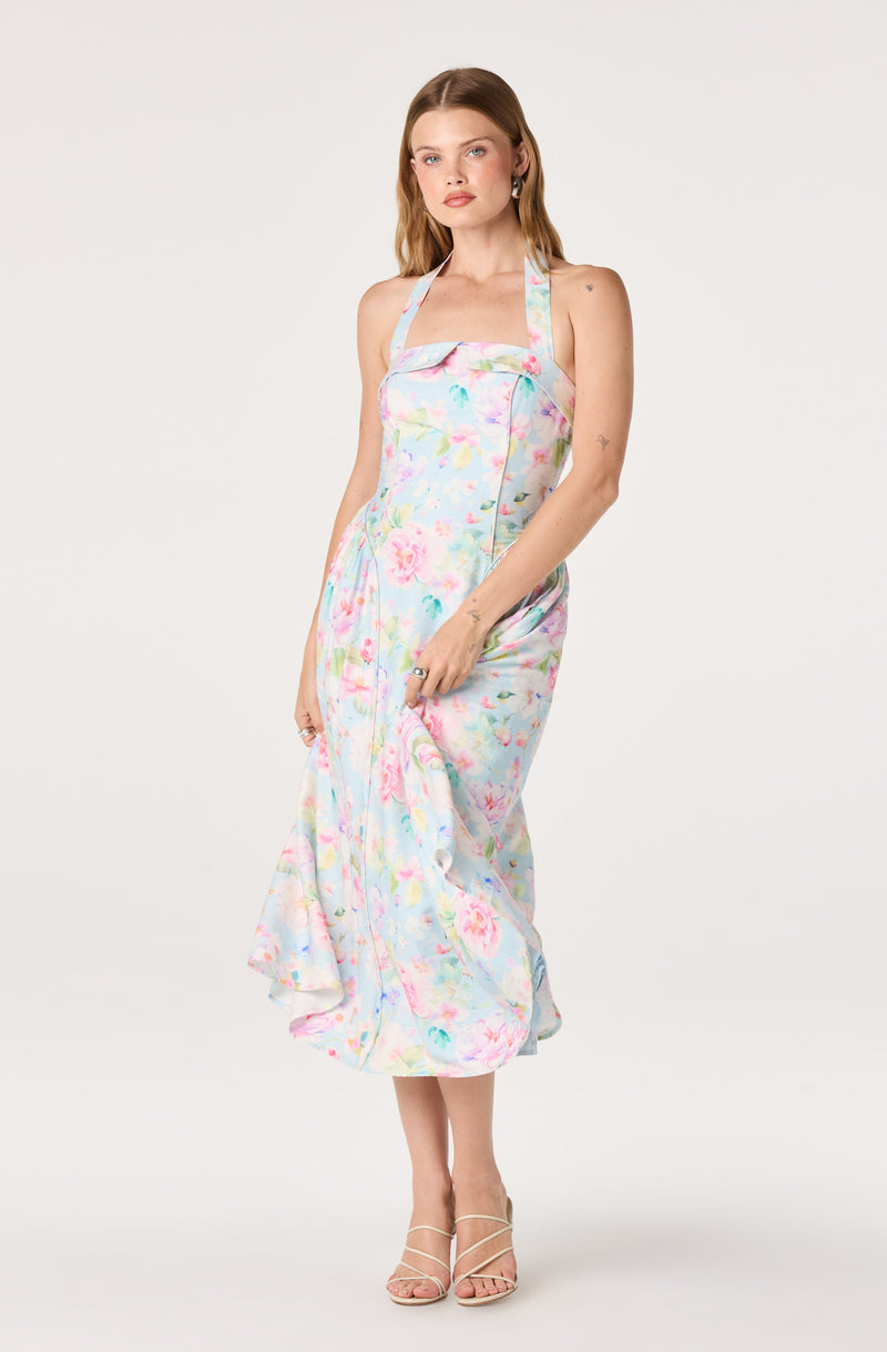 Woman wearing a pastel floral halter dress with a fitted bodice and flowing skirt.