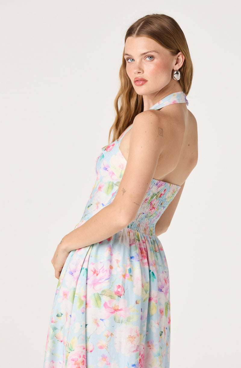 Woman in a colorful, sleeveless, floral dress with a halter neckline and gathered waist.