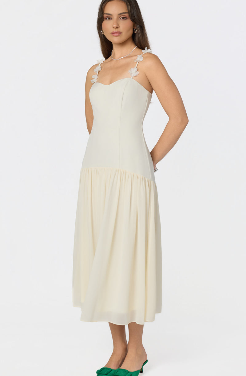 Woman wearing a sleeveless white dress with floral shoulder straps and green heels.