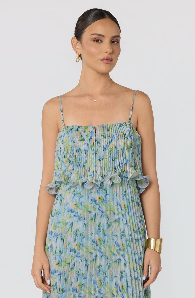 Woman wearing a light, flowy dress with a floral pattern, spaghetti straps, and ruffled details.