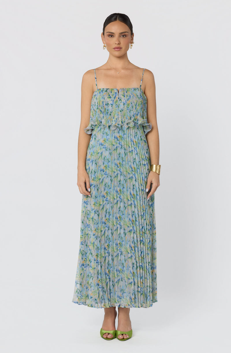 Woman wearing a spaghetti strap, floral printed maxi dress with ruffled overlay, in shades of blue and green.