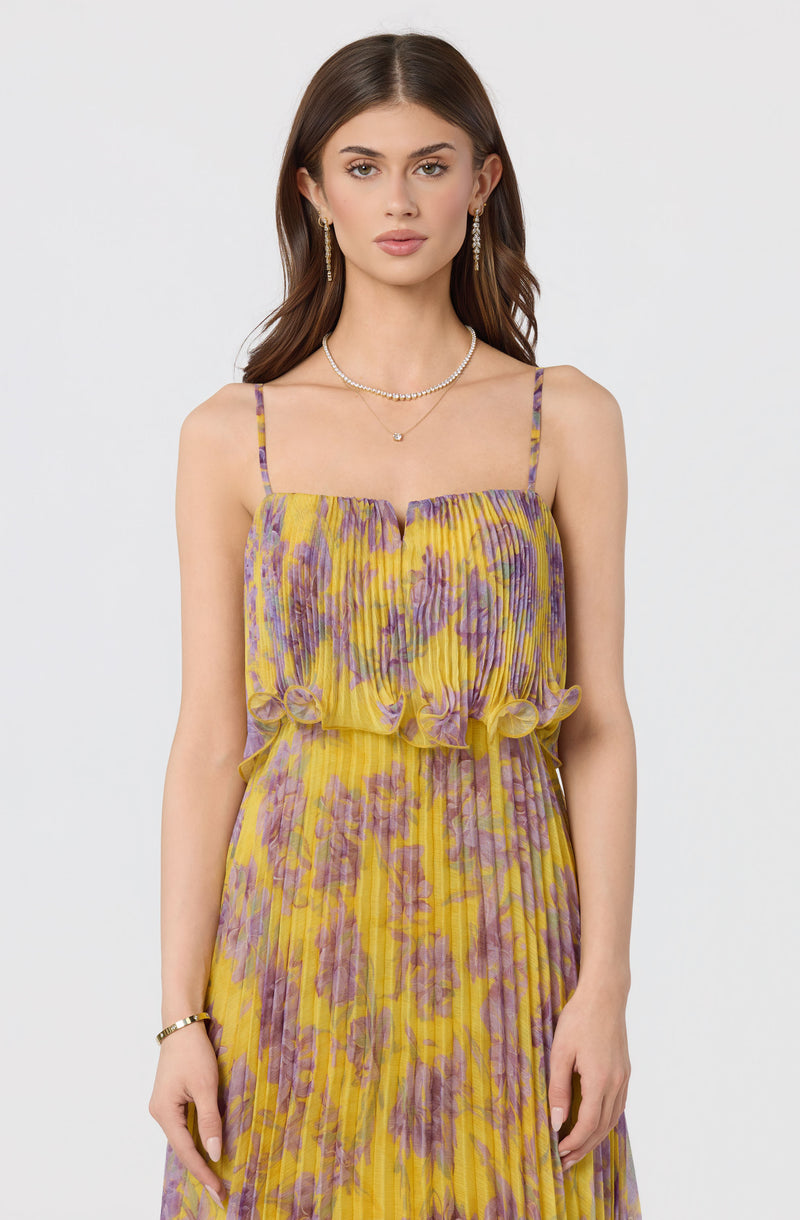 Woman wearing a yellow and purple floral sleeveless dress with spaghetti straps.