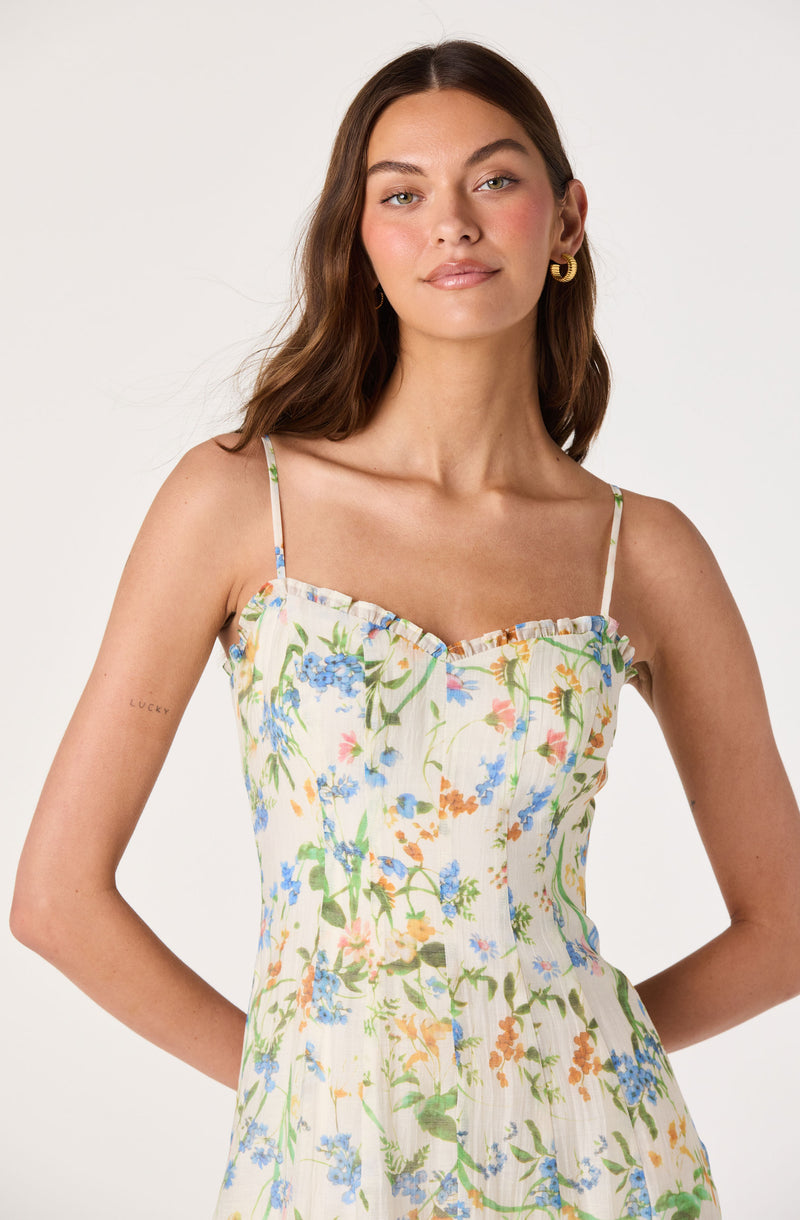 Woman wearing a white dress with colorful floral print and thin spaghetti straps.