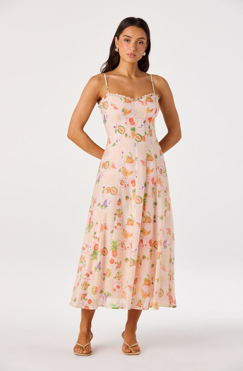 Woman in a pink, colorful printed maxi dress with spaghetti straps and flat sandals.