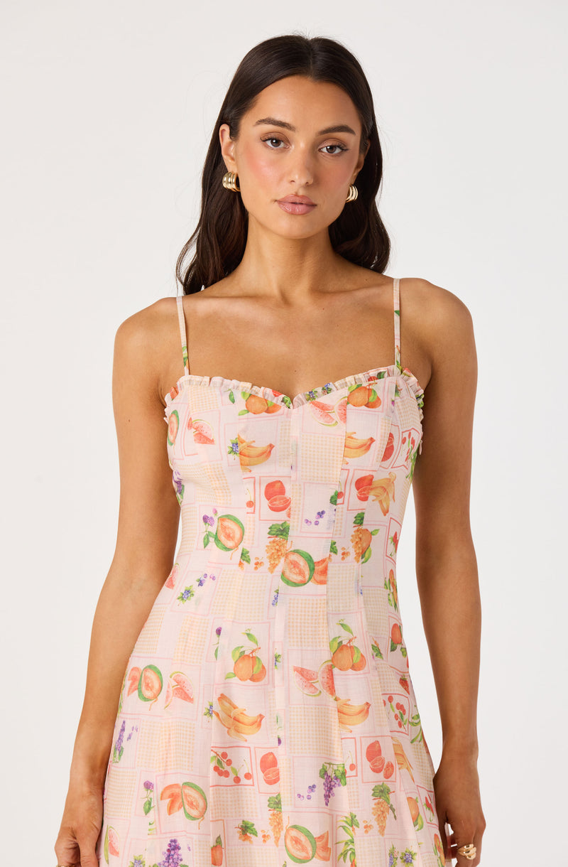 Sleeveless dress with a colorful fruit and floral print on a pink and peach checkered background.